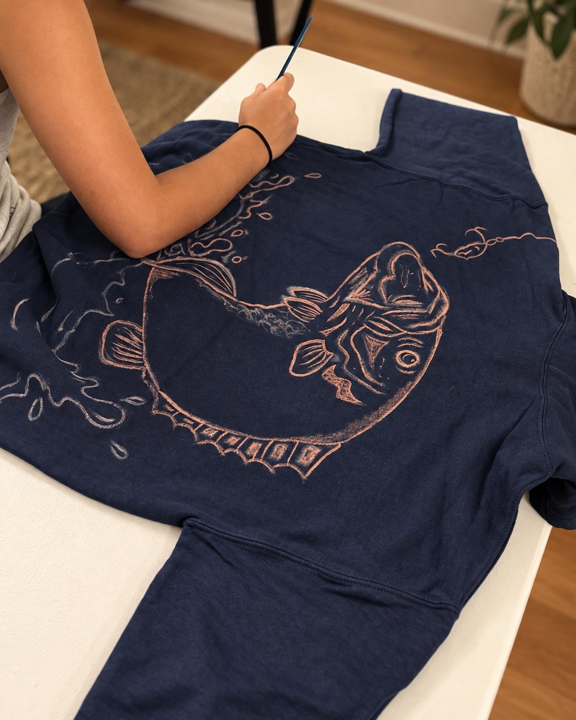 Hand-painting a fish design with bleach on a navy garment